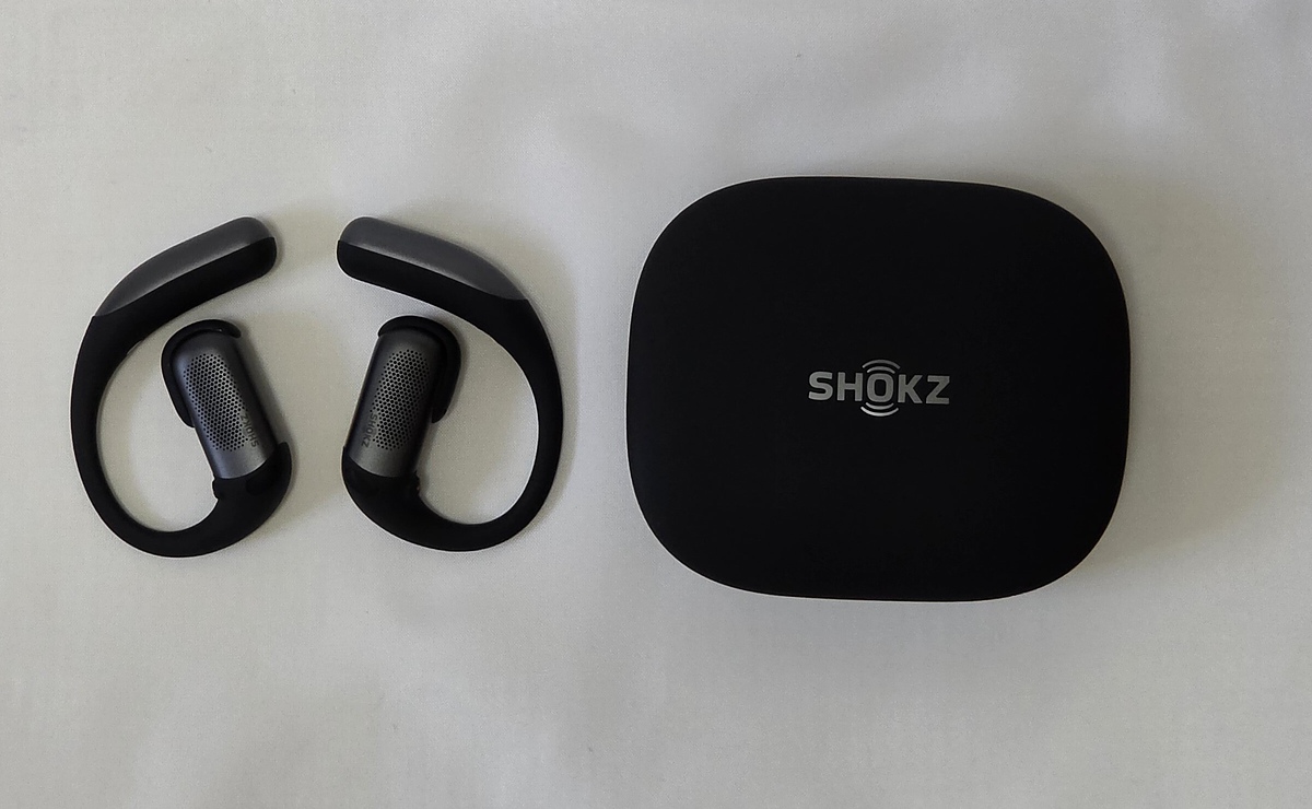 Shokz OpenFit Proのイヤホン本体と充電ケース。左に耳掛け式のイヤホンが2つ、右にSHOKZロゴの入った黒い充電ケース
